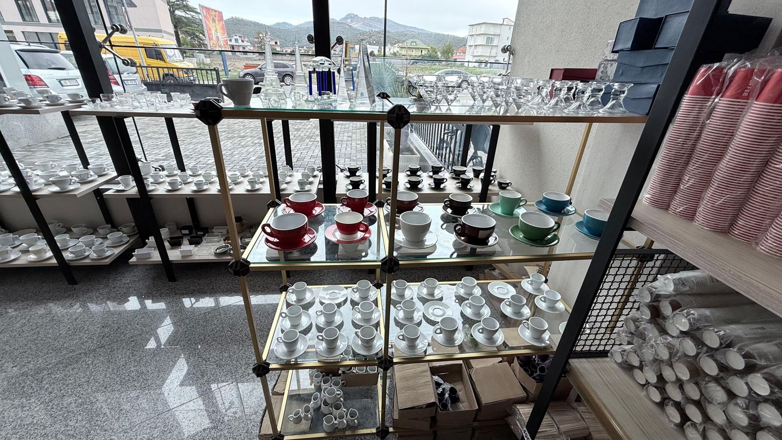 Filxhanë të kuq, kafe, jeshil e blu dhe filxhanë të bardhë në raft xhami